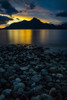 Golden sunlight glowing behind a silhouetted mountain and a tranquil lake with rocky shore in the foreground; Vancouver, British Columbia, Canada Poster Print by Aaron Von Hagen / Design Pics - Item # VARDPI12514597