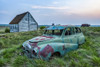 Vintage car sitting in the overgrown grass in a field with old buildings on a farmstead; Saskatchewan, Canada Poster Print by Robert Postma (19 x 12) # 12577829