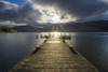 Wooden jetty on lake with dramatic clouds at sunrise at Loch Lomond in Scotland, United Kingdom Poster Print by Raimund Linke (19 x 12)