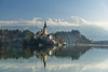 Looking across the calm waters of Lake Bled at dawn to the church on Lake Bled Island and Bled Castle behind; Bled, Slovenia Poster Print by Ian Cumming (20 x 13)