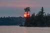 Vibrant sun glowing over tranquil lake and forest at sunset and sunbeam reflected on water, Lake of the Woods, Ontario; Kenora, Ontario, Canada Poster Print by Keith Levit (20 x 13)