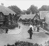 Historic image in black and white of thatched cottages on the Isle of Wight, with a postman,pedestrians and a horse and carriage on the street, circa 1900; Isle of Wight, England Poster Print by John Short (17 x 16)