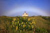 Coquille River Light on the Oregon coast with grasses and wildflowers in a field in the foreground and a faint rainbow in the sky over the lighthouse; Bandon, Oregon, United States of America Poster Print by Craig Tuttle (17 x 11)