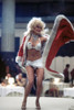 Judy Landers dancing on a table, wearing a red cape, diamond bikini top and sarong, 1970s. Photo: Oscar Abolafia (judylanders003) Poster