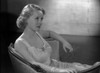 Bette Davis Seated on a Couch with Arms Rested on the Edge of the Chair while Holding a Lighted Cigarette in White Silk Dress Photo Print - Item # VARCEL692796