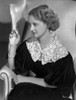 Bette Davis Seated on White Couch with Cigarette on Hand in Black Dress with White Lace Collar Photo Print - Item # VARCEL692870