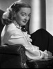 Bette Davis Seated on a Black Leather Couch in White Long Sleeve Dress with White scarf and Black Neckerchief Photo Print - Item # VARCEL693267