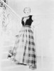 Bette Davis Posed on the Staircase with Hand on the Waist in Black Sheer Sleeveless Top and Gingham Long Skirt Photo Print - Item # VARCEL693431