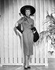 Jane Wyman Posed in Grey Short Sleeve Folded Top Silk Dress and Black Velvet Gloves with Black Hat while Right Hand Placed on the Back Photo Print - Item # VARCEL705838