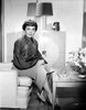 Jane Wyman Seated on the Couch in Black Pleated Long Sleeve Silk Dress and Tweed Linen Skirt with Necklace with Hands on the Lap and Legs Crossed Photo Print - Item # VARCEL705878