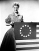 Jan Sterling Posed in Velvet Long Sleeve Dress and Accordion Pleated Skirt while Holding a Flag Photo Print - Item # VARCEL706492