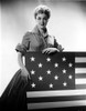 Jan Sterling Posed in Velvet Shirt and Pleated Skirt with Rolled Up Sleeves while Holding a Flag Photo Print - Item # VARCEL706494