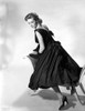 Vera Miles kneeling onto a chaise lounger, looking behind her shoulder, wearing a black, sleeveless gown with bows elegantly placed along the back Photo Print - Item # VARCEL706571