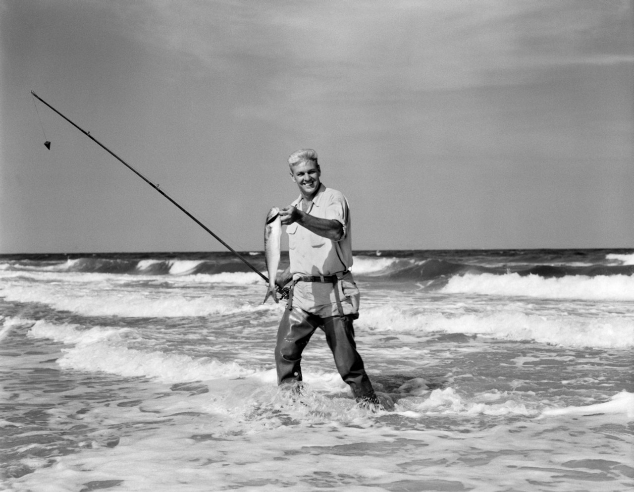 1950s Older Man Standing In Surf In Waders Holding Fish In One