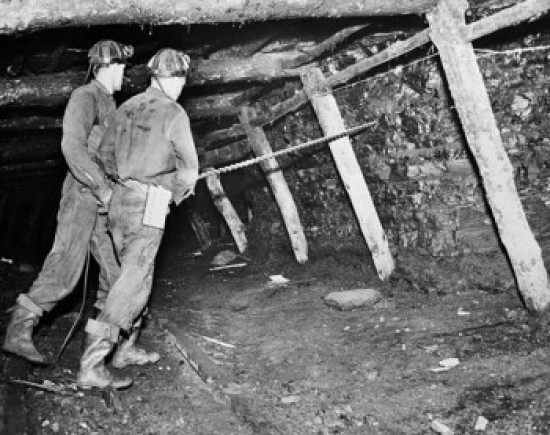 Side profile of two coal miners drilling in the wall of a pit mine