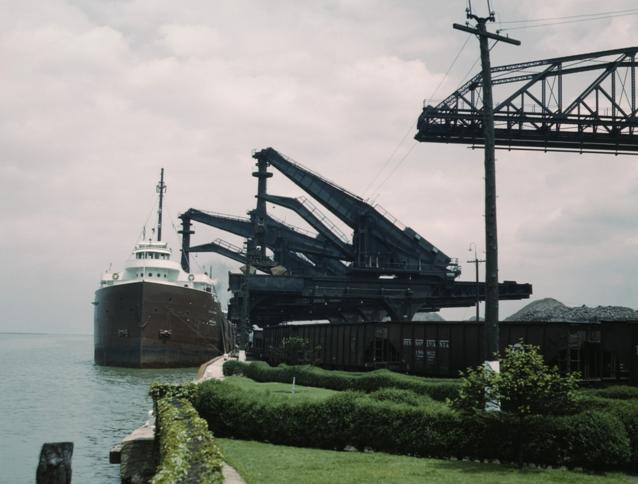 Great Lakes Freighter Unloading Iron Ore At The Pennsylvania Railroad Ore  Docks In Cleveland Ohio. One 'Hulett' Unloader Is Lowering Its Bucket Into 