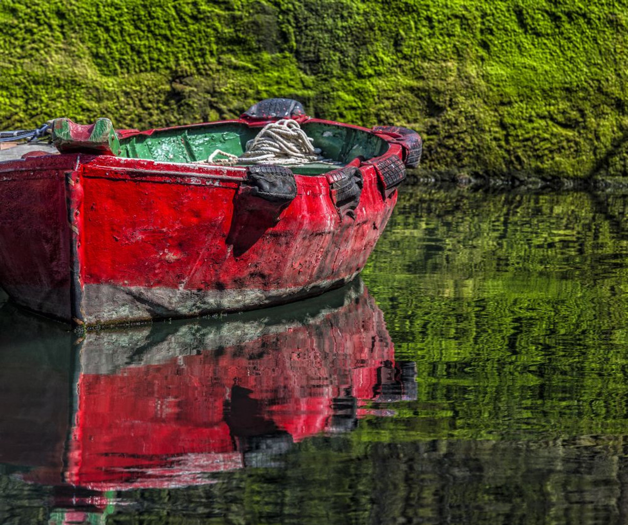 Small, wooden fishing boat moored to the shore with a mirror image