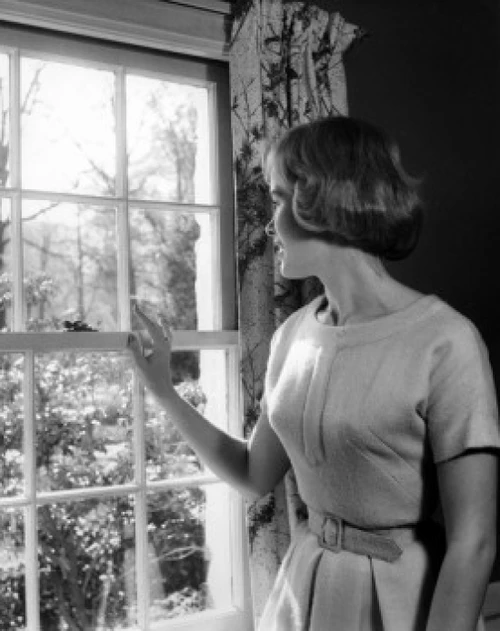 Young woman looking through window Poster Print