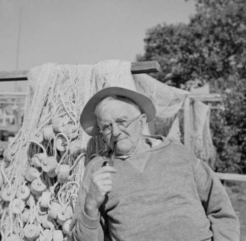 Senior man wearing hat and smoking pipe  fishing nets in the background Poster Print - Item # VARSAL255421645
