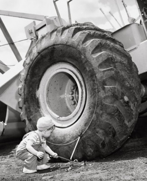 Boy holding a tool and crouching near a bulldozer Poster Print - Item # VARSAL25512871