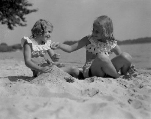 Two girls playing in sand on beach Poster Print
