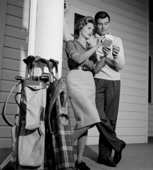 Mid-adult couple examining tickets with golf trolleys standing against column Poster Print - Item # VARSAL255417151