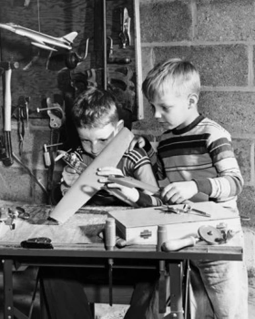 Boy making a model airplane with another boy looking at him Poster Print