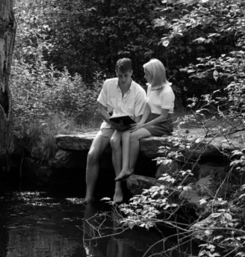 Young couple sitting by pond Poster Print