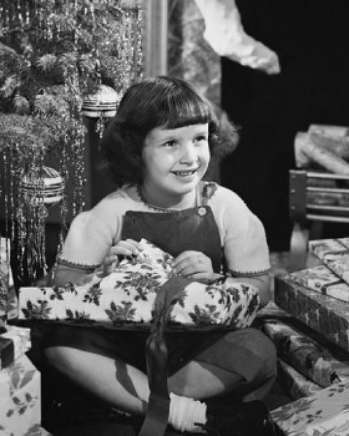 Girl sitting near a Christmas tree and opening a Christmas present Poster Print - Item # VARSAL25526691