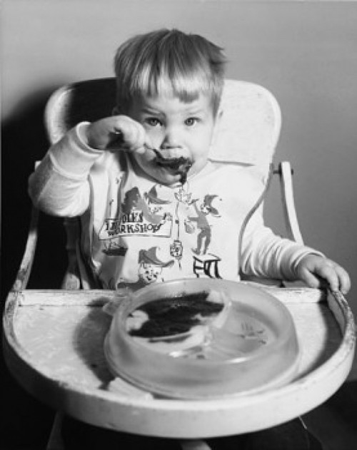 Baby sitting in a high chair and eating baby food Poster Print