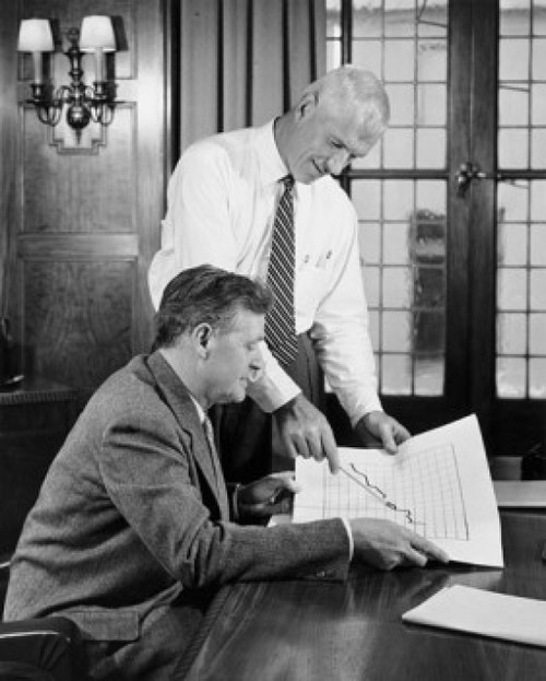 Two businessmen discussing line graph in office Poster Print