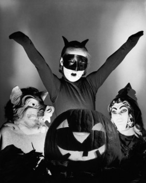 Close-up of an illuminated jack o' lantern with three people wearing Halloween costumes behind it Poster Print - Item # VARSAL25518807
