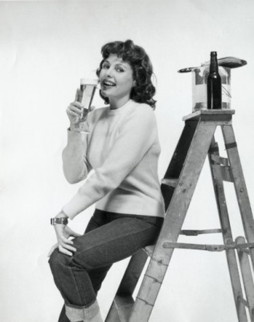 Portrait of a young woman sitting on a step ladder and drinking beer Poster Print