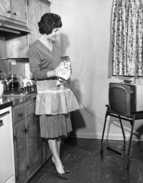 Side profile of a young woman looking at a television in the kitchen Poster Print