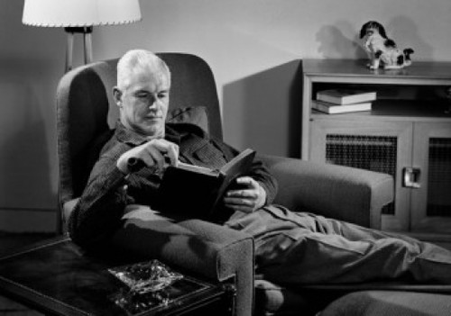 Senior man sitting in armchair and reading book Poster Print