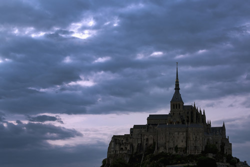 Silhouette of large stone Abbey perched on rocky hill with dramatic clouds at sunset; Mont St. Michel, Brittany, France PosterPrint - Item # VARDPI12282603