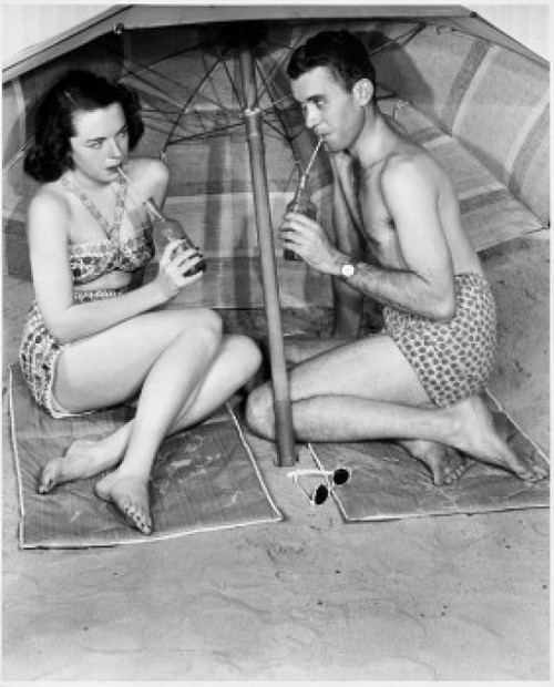 Young couple sitting under beach umbrella drinking Poster Print - Item # VARSAL2556623