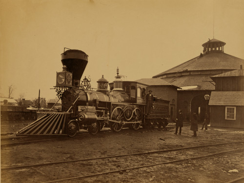 Ornately decorated locomotive J.H. Devereux, of the United States Military Railroad with two crew members on board outside the roundhouse at the Alexandria station. Poster Print - Item # VARBLL058745609L