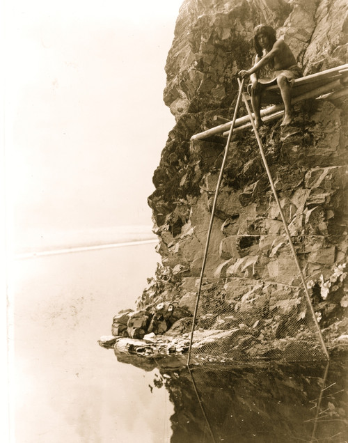 Hupa man sitting on a platform on a rocky cliff, handling a fishing net. Poster Print - Item # VARBLL058746939L