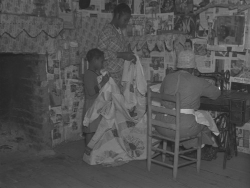 African American Mother Is Assisted By Her Two Daughters As She Sews A Quilt In Their Newspapered Home On The Pettway Plantation In Gees Bend History - Item # VAREVCHISL009EC089