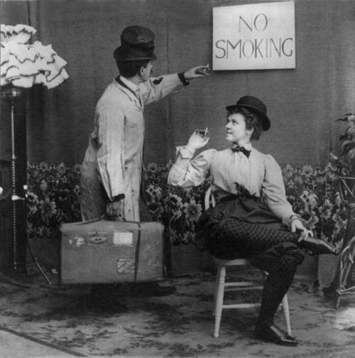 Humorous Scene Of Man Pointing To No Smoking Sign Above Woman In Derby And Bloomers Who Is Smoking Cigarette History - Item # VAREVCHCDLCGCEC090