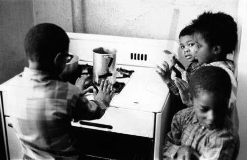 Four African American Children Cluster Around The Gas Stove For Warmth. The Inadequate Heating In Their Harlem Apartment Encourages Use Of The Dangerous Alternative When Heat Is Not Provided By Slum Landlords. April 6 History - Item # VAREVCCSUA000CS
