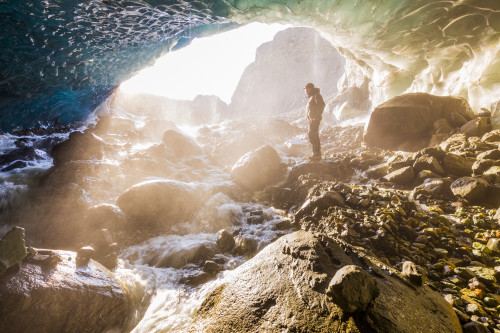 A man stands at the entrance of an ice cave bathed in warm sunlight and mist, Wrangell-St. Elias National Park; Alaska, United States of America Poster Print by Steven Miley / Design Pics - Item # VARDPI12435675