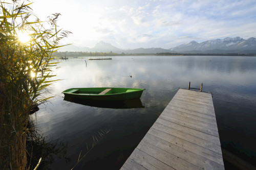 Wooden Jetty with Rowboat and Sun, Hopfen am See, Lake Hopfensee, Bavaria, Germany Poster Print by Raimund Linke (19 x 12)