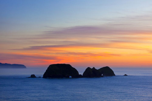 Winter sunset and silhouetted rock formations with natural arches, viewed from Cape Meares on the Oregon coast, USA; Oregon, United States of America Poster Print by Craig Tuttle (17 x 11)