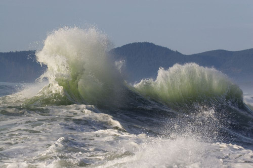 Splashing wave as it breaks at the shore with the Oregon coastline in the background at Cape Kiwanda; Oregon, United States of America Poster Print by Craig Tuttle (17 x 11)