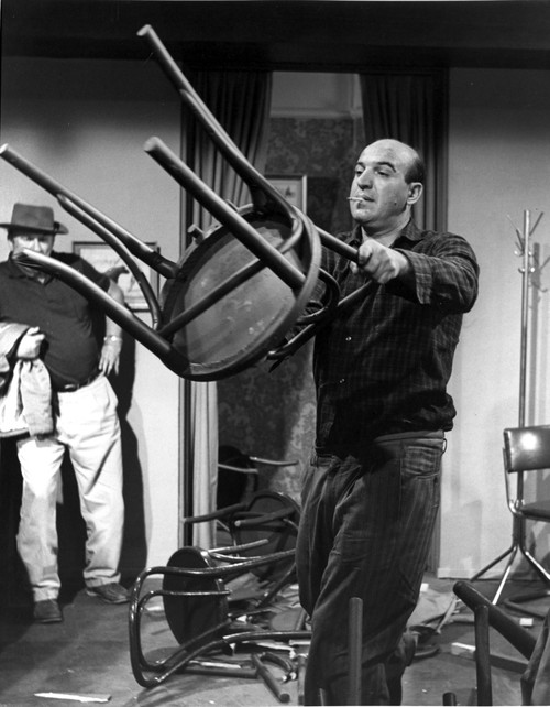 Telly Savalas lifting a chair Photo Print - Item # VARCEL684150
