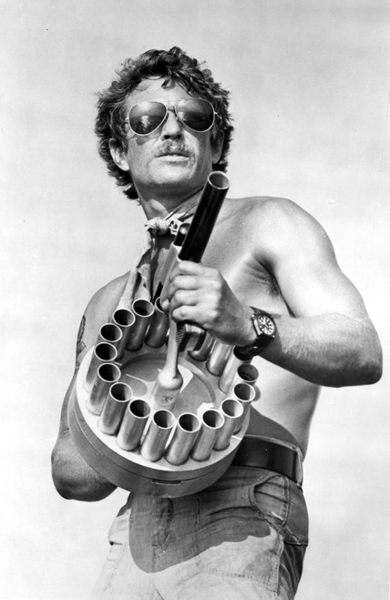 Tom Berenger carrying a machine gun and wearing aviator sunglasses Photo Print - Item # VARCEL684920