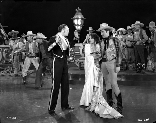 Bebe Daniels standing in White Long Dress while Two Men in Cowboy Outfit and Matador Outfit standing Beside Her Photo Print - Item # VARCEL696680