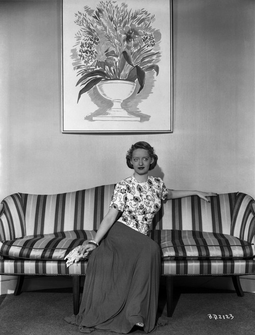 Bette Davis Seated on a Striped Couch in High Neck Short Sleeve Floral Dress and Silk Skirt Photo Print - Item # VARCEL692996